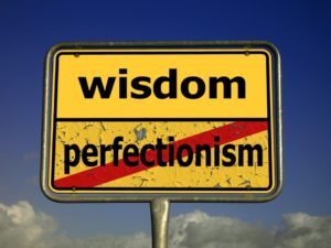 road sign that says wisdom with the word perfectionism crossed out